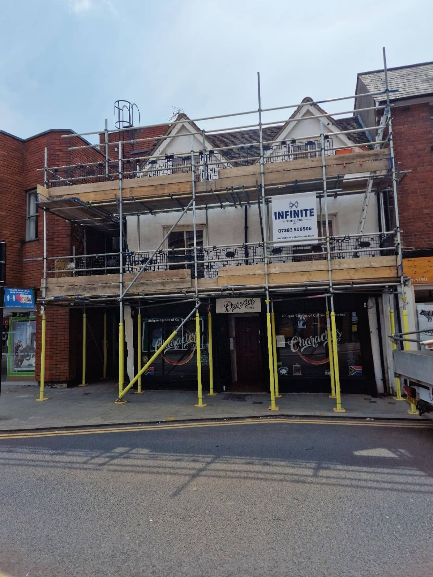 Commercial scaffold with Infinite Scaffolding site board on a high-street property